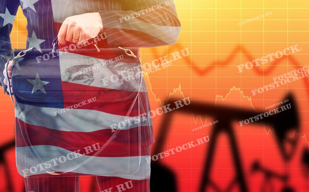 На фото изображен бизнесмен с портфелем, на котором изображен американский флаг, на фоне графика и нефтяных вышек. Это символизирует влияние колебаний цен на нефть на экономику Соединенных Штатов.
